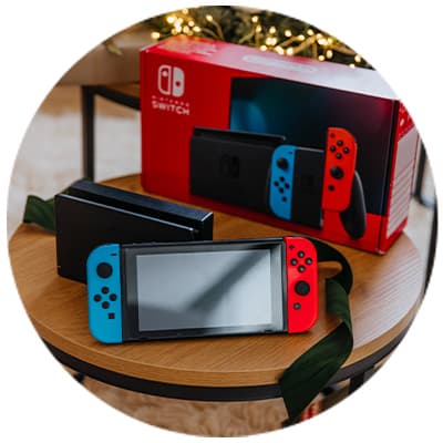 Nintendo Switch-Konsole mit blauen und roten Joy-Cons auf Tisch, Verpackung im Hintergrund, Weihnachtsbeleuchtung