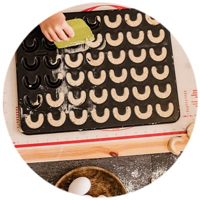 Hand verteilt Mehl auf Kipferl in Backform, Eier und Teigrolle auf Arbeitsfläche