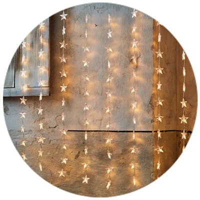 Sternförmige Lichterketten hängen vor einer hellen Wand und leuchten warm