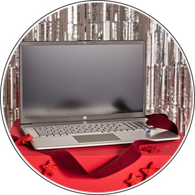 Silberner Laptop auf rotem Tisch, dekoriert mit roten Sternen und Band, vor silbernem, glitzerndem Hintergrund