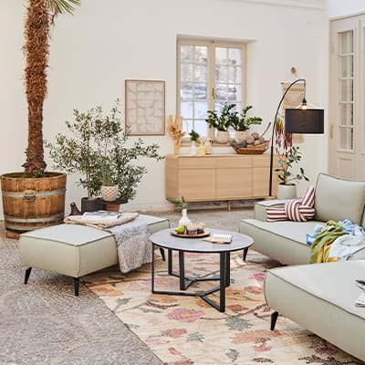 Modernes Wohnzimmer mit grünen Möbeln, Teppich, Pflanzen und Dekoration auf Sideboard und Tisch.