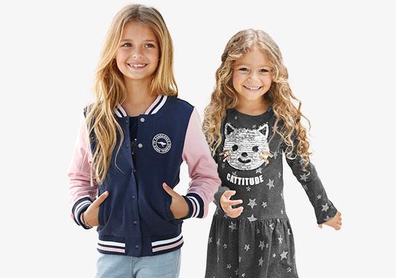 Zwei Mächen in modischer Kleidung: Das linke Kind trägt eine blaue Collegejacke mit rosa Ärmeln, das rechte Kind ein graues Kleid mit Sternenmuster und einem Katzenmotiv