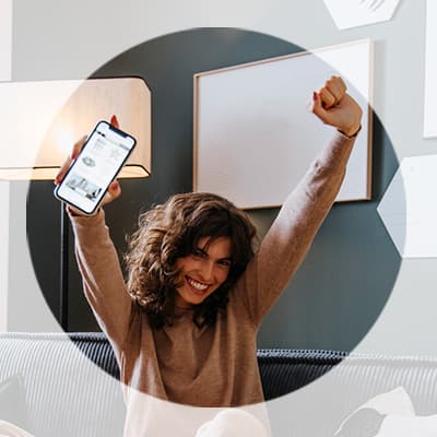 Frau sitzt auf dem Sofa, hält ihr Smartphone hoch und reißt jubelnd beide Arme in die Luft