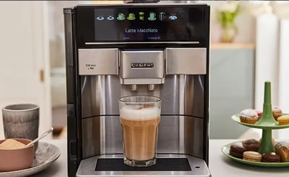 Latte Macchiato auf Display – Siemens Kaffeemaschine bereitet Latte Macchiato zu, daneben eine Schale mit Zucker und eine Etagere mit Macarons