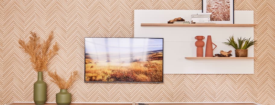 Wand mit gemustertem Tapeten, TV mit Landschaftsbild, zwei Regale mit Deko, darunter Vasen mit getrockneten Pflanzen