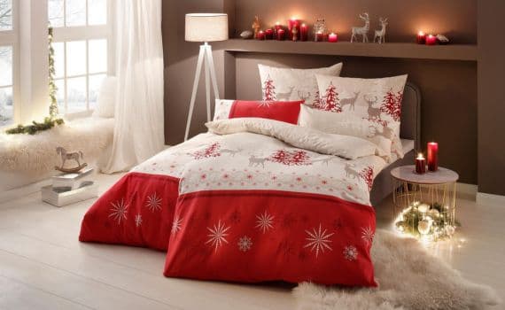 Bettwäsche mit roten und weißen Weihnachtsmotiven, Schneeflocken und Rentieren, festlich dekoriertes Schlafzimmer mit Kerzen und Lampen