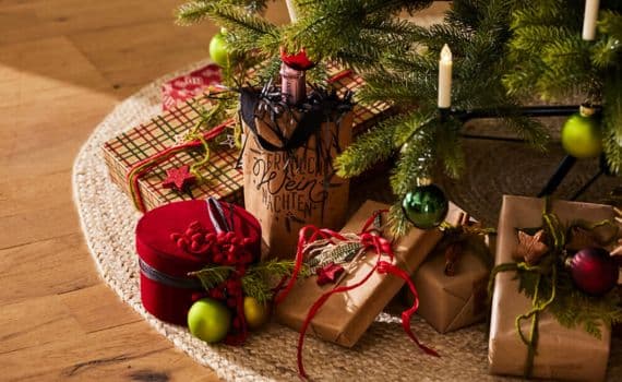 Geschenke unter einem Weihnachtsbaum, darunter eine Flasche Wein mit der Aufschrift "Fröhliche Weihnachten"