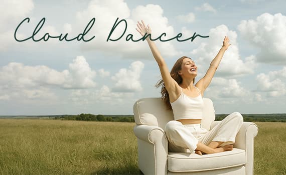 Cloud Dancer – Frau in weißem Top und Hose sitzt mit erhobenen Armen auf einem Sessel im Freien