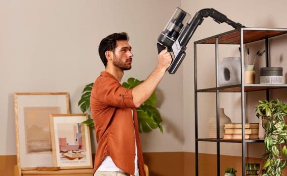 Mann reinigt mit einem Staubsauger ein Regal im Wohnzimmer.